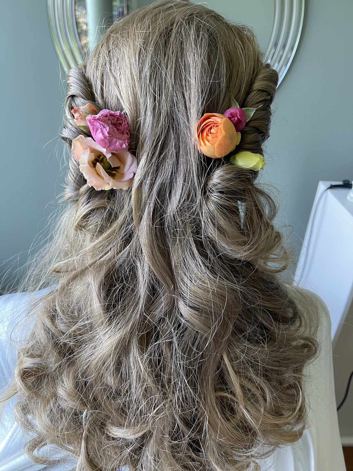Brudefrisyre med rosa og oransje blomster festet i løse krøller