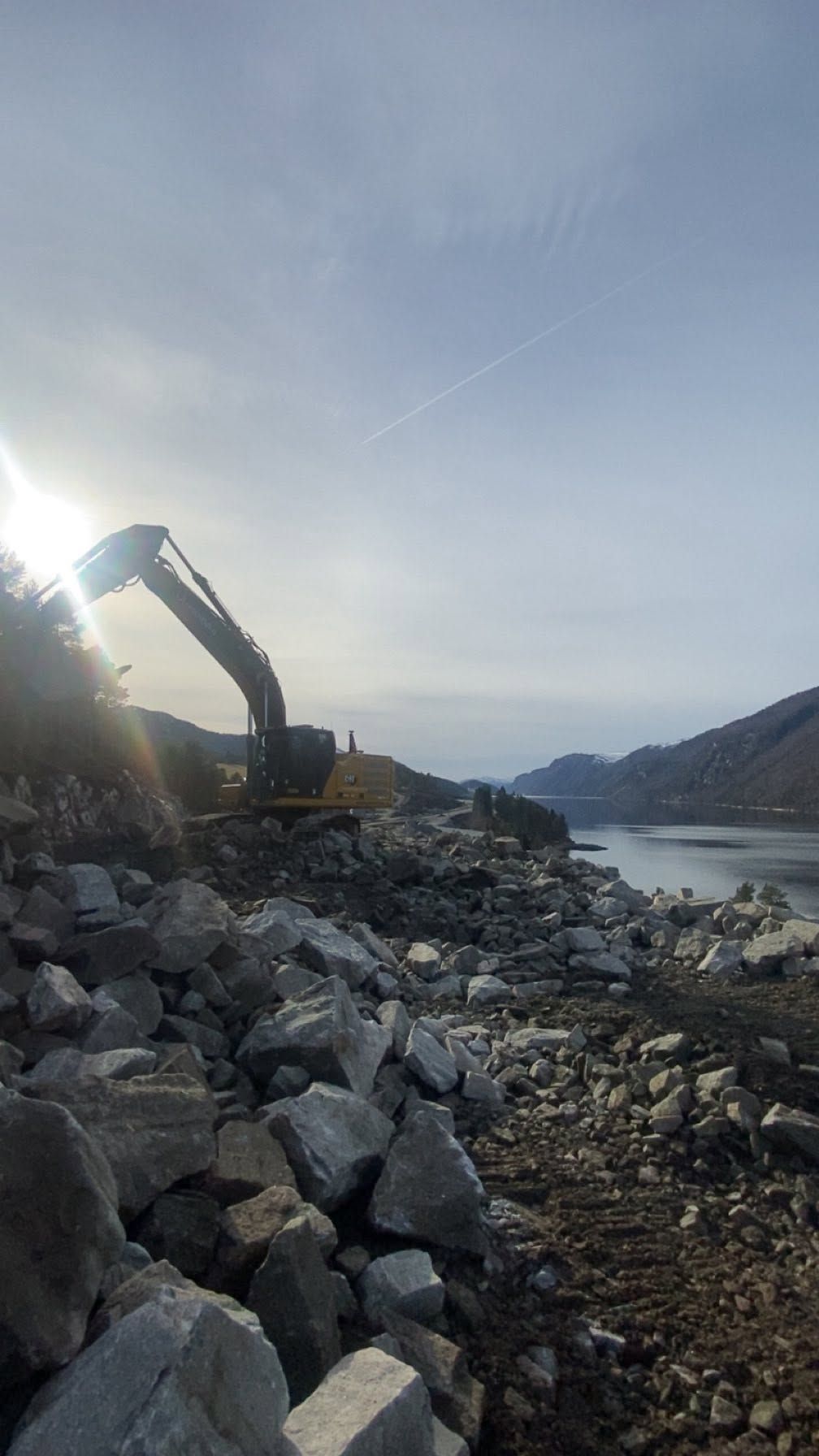 Veibygging langs fjorden med gravemaskin i steinfylling