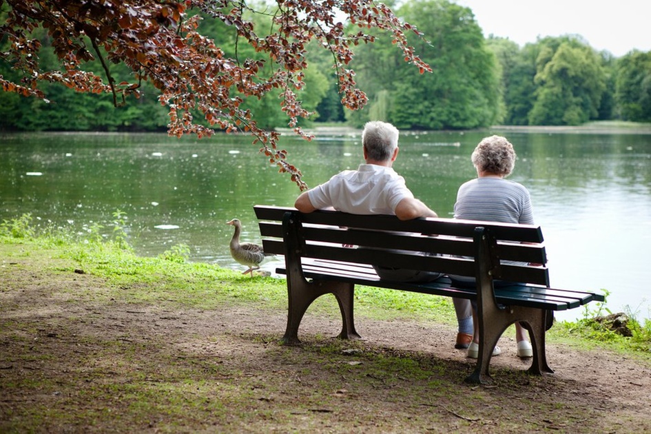 To eldre personer på en benk i parken ved et tjern. Vi tilbyr privat hjemmehjelp i Oslo og Akershus.