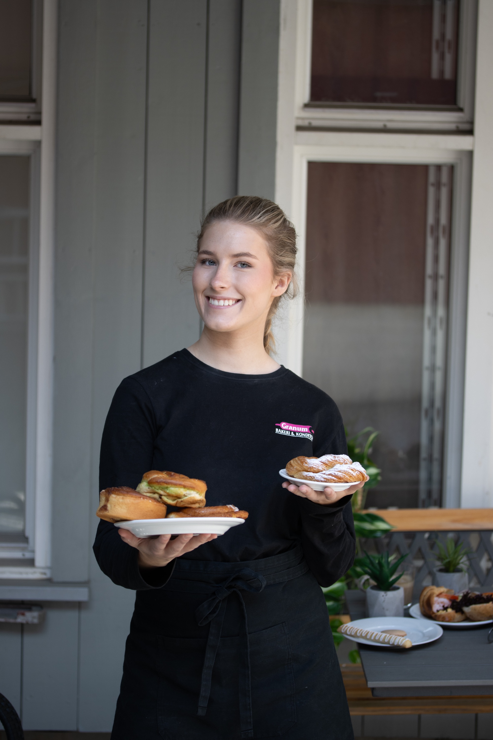 Smilende ansatt fra Granum Bakeri med ferske bakevarer på fat