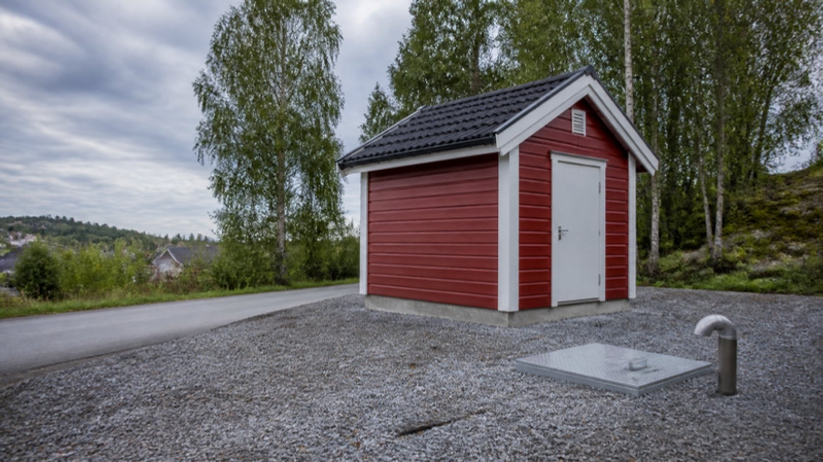 Illustrasjonsbilde av et rødt pumpehus over en nedgravd pumpestasjon ved en vei