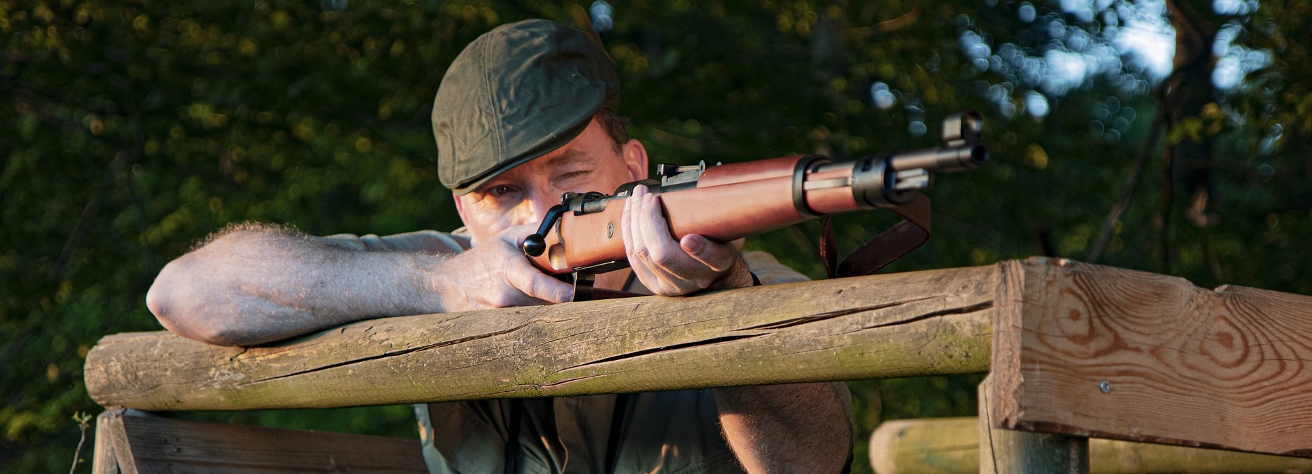 Jeger sikter med rifle over en skyteplattform i skogkanten