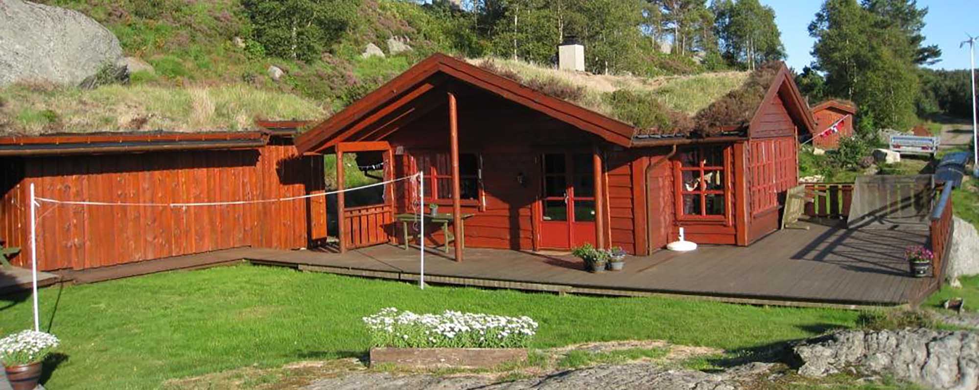 Rød hytte med torvtak, terrasse og hage