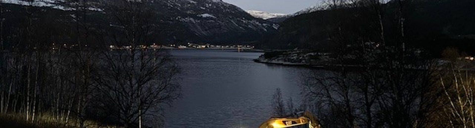 Anleggsmaskin i arbeid i skumringen ved fjorden
