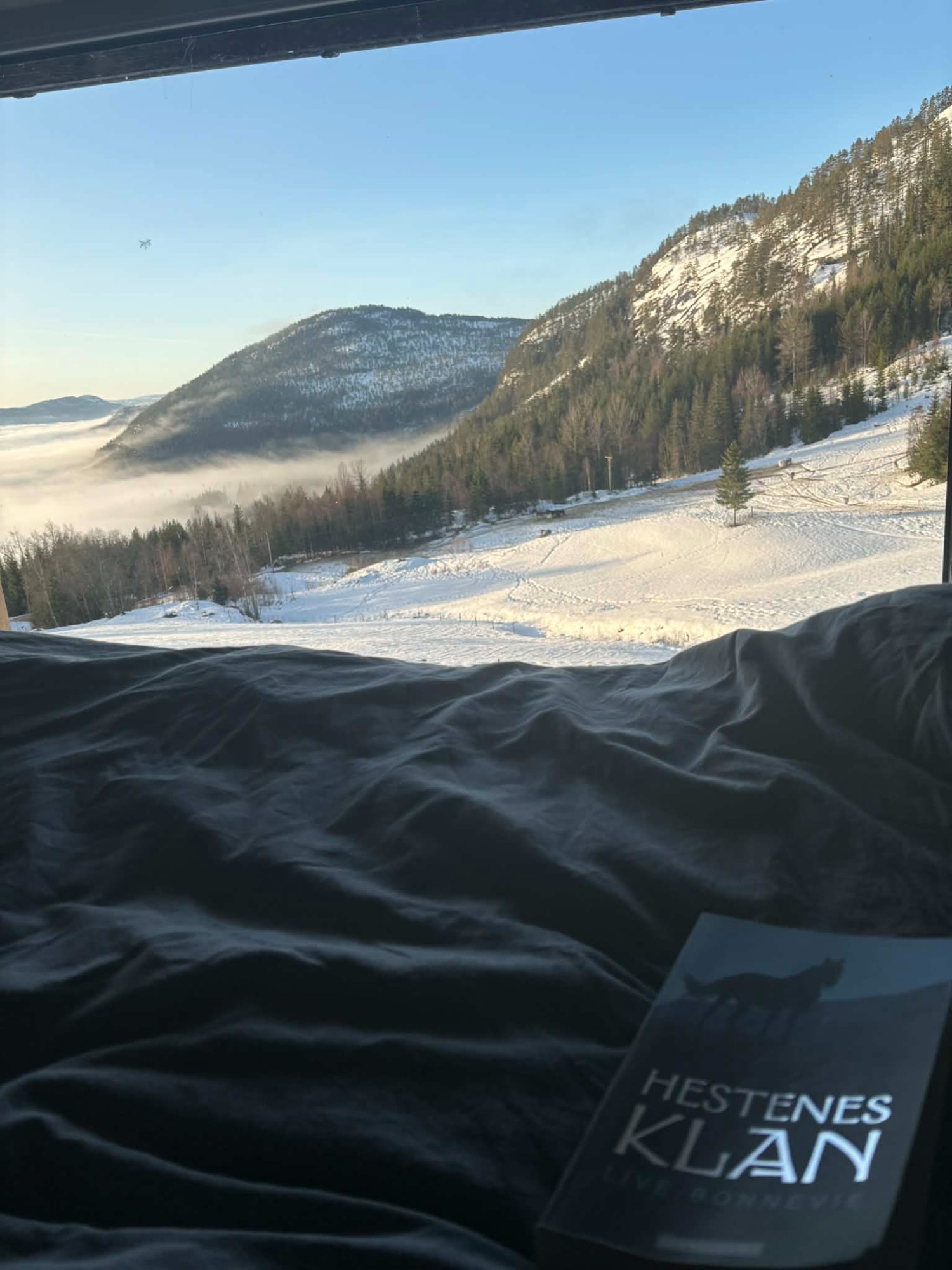 Panoramaleiligheten – utsikt fra sengen med tåke i dalen, snødekte fjell og Hestenes Klan-sengetøy