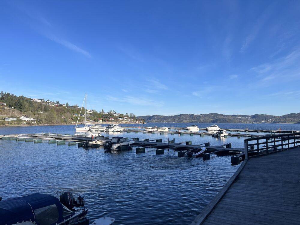 Flytebrygger med fritidsbåter ved Havnevik Brygge, rolig fjord og åser i bakgrunnen
