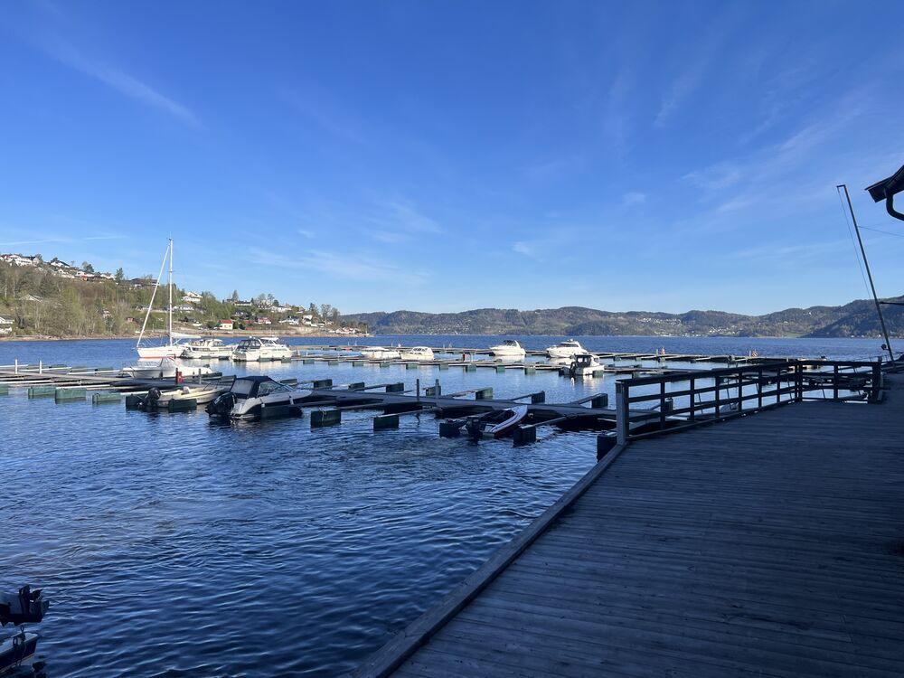 Utsikt fra brygga over flytebrygger og fjorden med fjell i horisonten