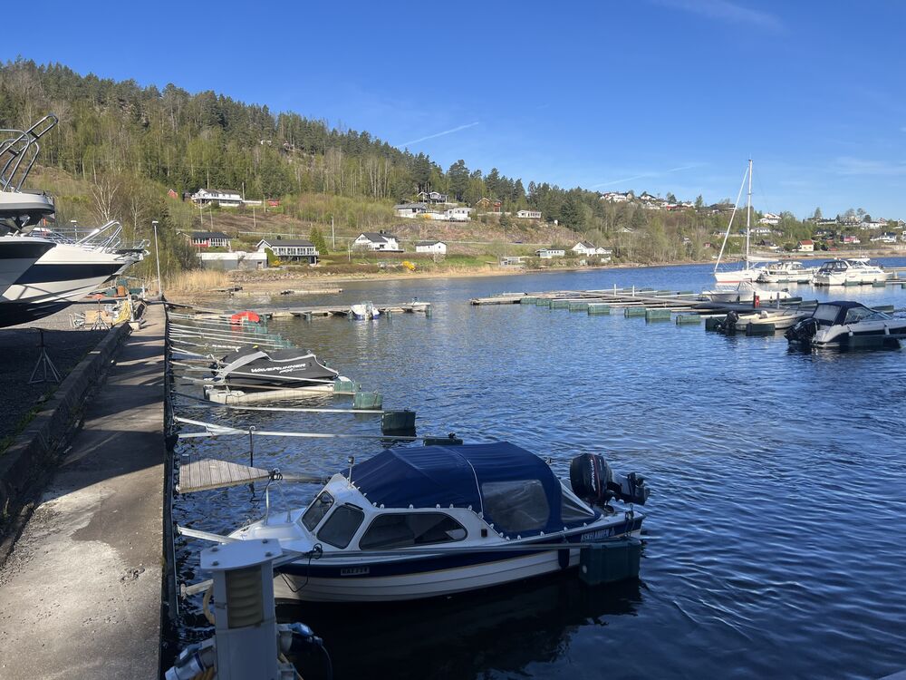 Båter fortøyd langs kaikanten ved Havnevik Brygge med bolighus og skog i bakgrunnen