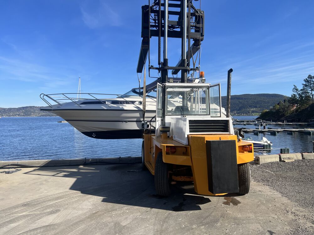 Kabinbåt løftes av truck ved kaikanten, brygger og fjord i bakgrunnen