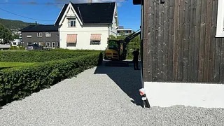 Gravemaskin på nyplanert grusplass ved et bolighus