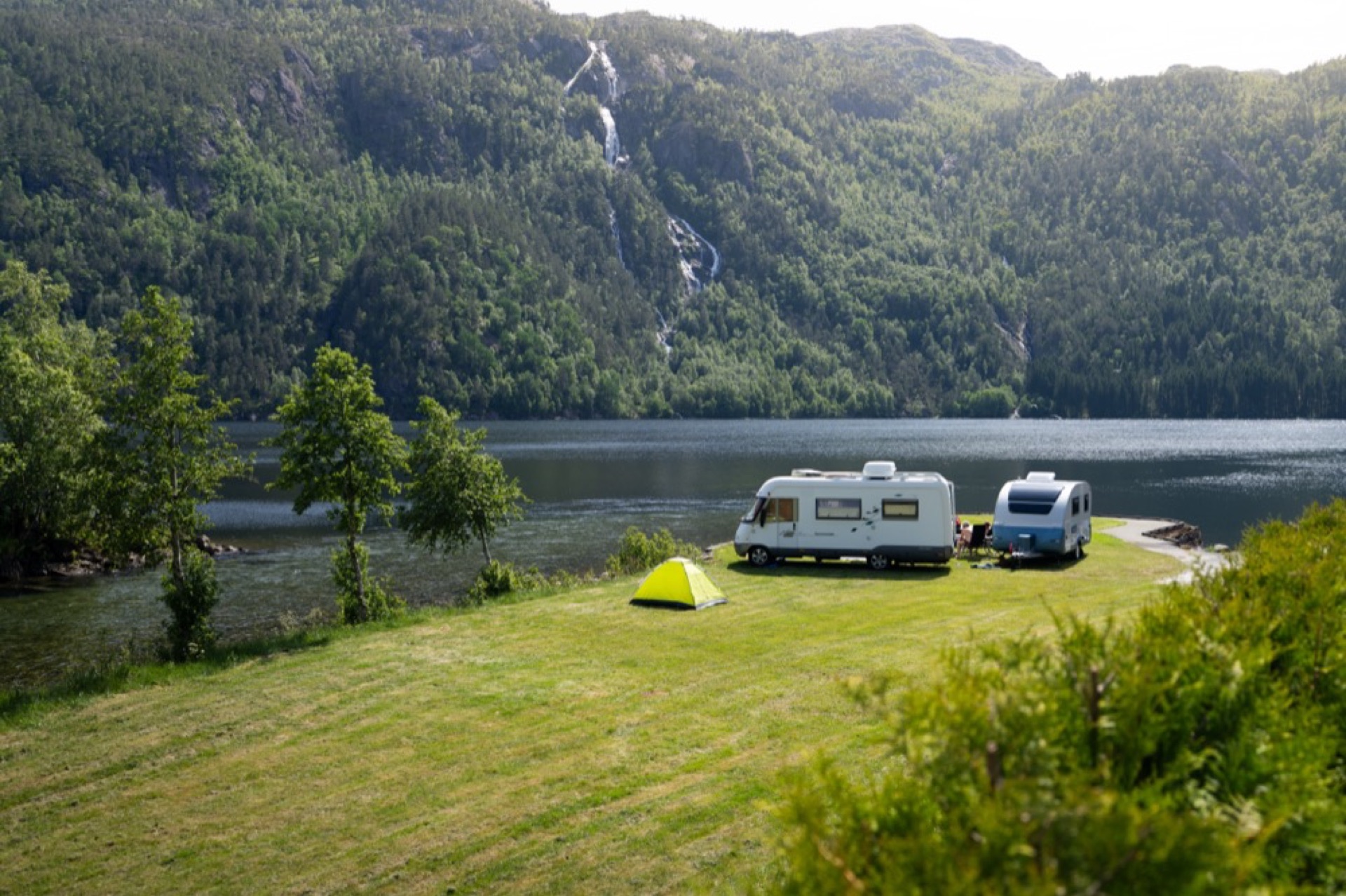 Bobiler og telt på gressletta ved fjorden
