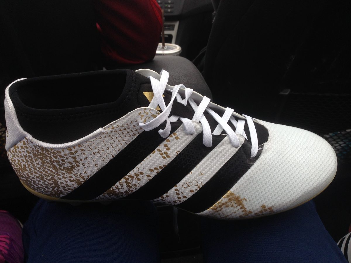 Hvit Adidas Ace-fotballsko med svarte striper og gullmønster
