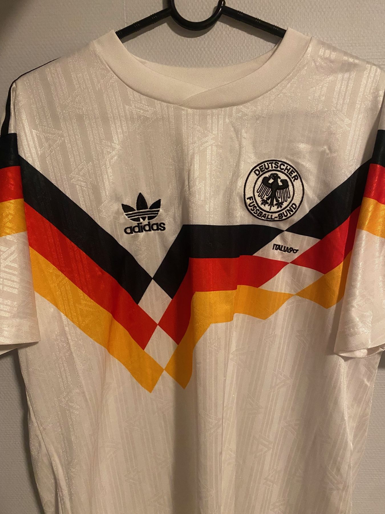 Hvit tysk landslagsdrakt fra VM 1990 sett forfra med svart, rødt og gult mønster over brystet