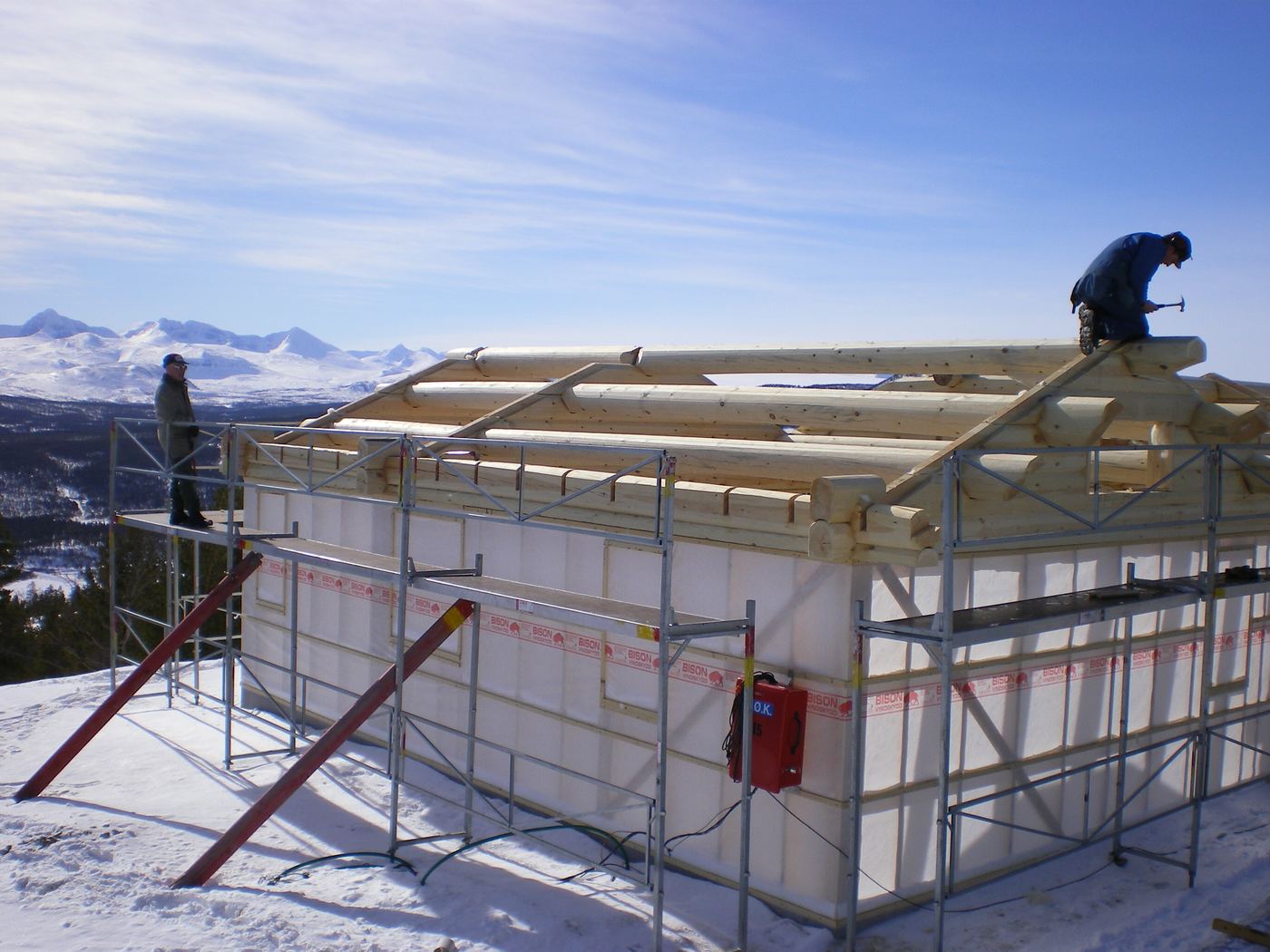 Laftehytte under oppføring med snødekte fjell i bakgrunnen