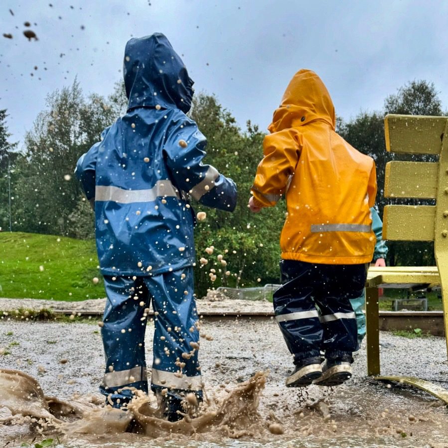 To barn i regnklær hopper i sølepytt