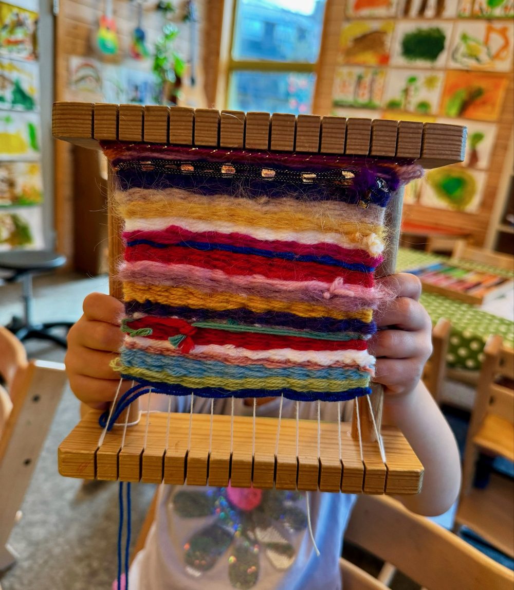 Barn viser stolt frem sin fargerike vev på vevramme