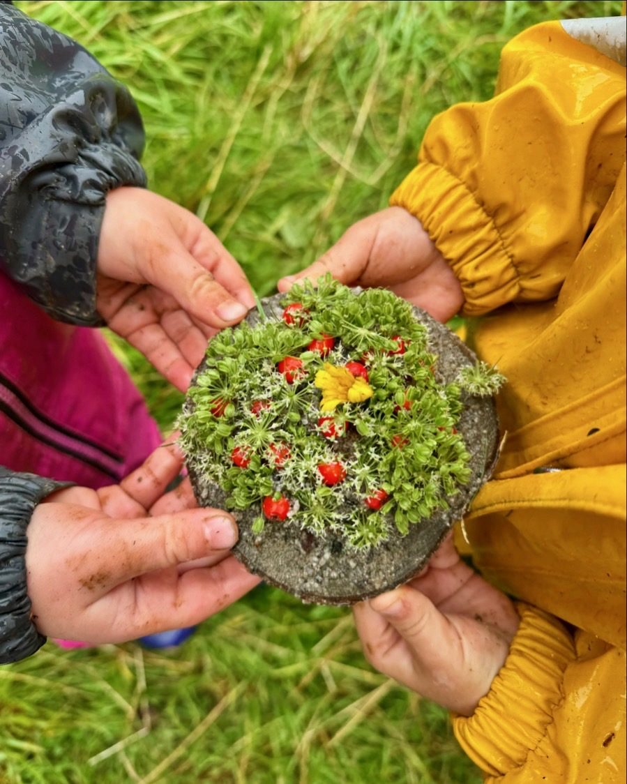 Barns hender holder stein dekorert med blomster og mose