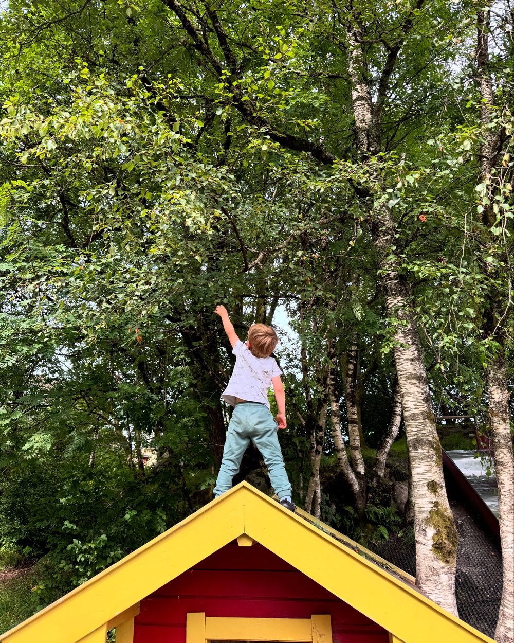 Gutt klatrer på toppen av lekehus i barnehagen