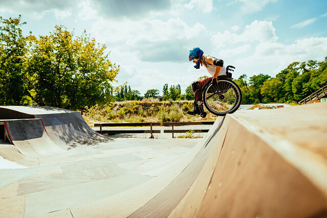 Ung kvinne i rullestol står på kanten av rampe i skatepark