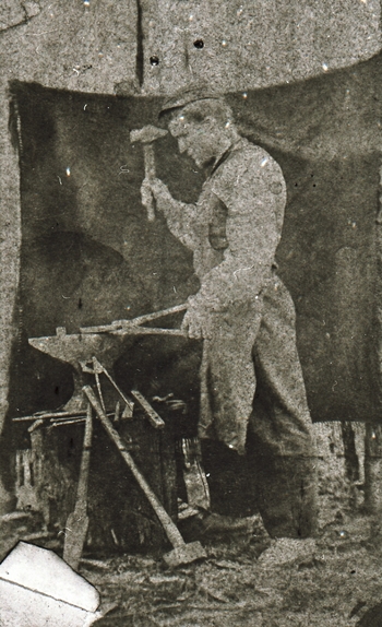 REF-0362. Smed i arbeid ved ambolten utendørs.
Bak på bildet står: K.Sundseth. Erindring til R. Øien.