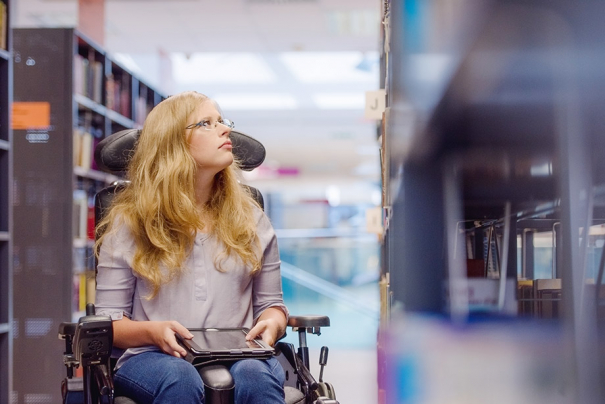 Ung kvinne i rullestol på bibliotek