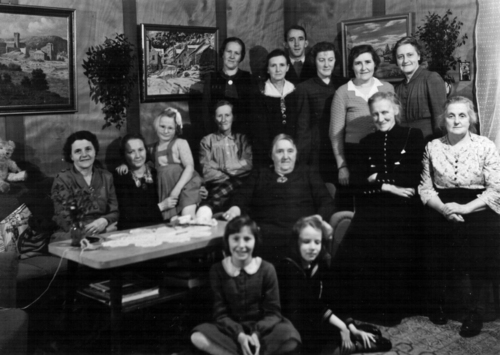 REF-0760 Reberg Gamle Prestegard, 1953.
Møte i Mærk Kvinneforening. Ved bordet: Edith Stubbråten, Johanna Fjelle, Jodda Sponås, Ingebjørg Lundaløkk, Anne Mærk. Sittende foran: Agnes Mærk, Sidsel Stubbråten. Stående bak: Emma Damli, Anne Voll, sokneprest Fritjof Stubbråten, Margit Bakk, Randi Sæther, Kohanna Aas. Sittende foran: Ragnhild Rogogjerd, Berit Sæther.