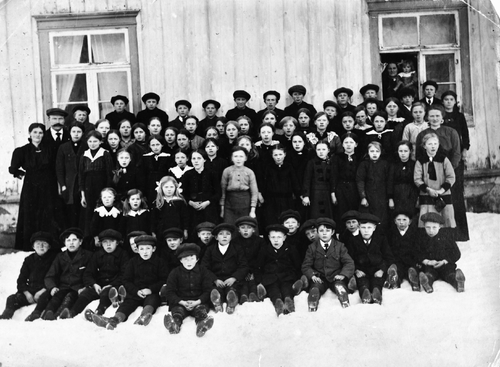 REF-0284 Voll skole/skule, Rennebu ca 1919 Bak t.v. lærar Nils Aarnes og kona Karen. Bak gutane står to av borna deira: Marit og Anna. Det tredje barnet som da var fødd, Gislaug, er hos bestemora i vindauget t.h..
