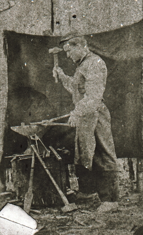 REF-0362. Smed i arbeid ved ambolten utendørs.
Bak på bildet står: K.Sundseth. Erindring til R. Øien.