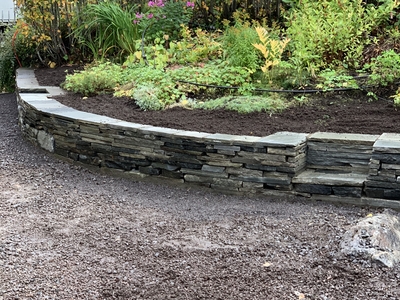 Skifer mur rå kopp med blomsterbed bak